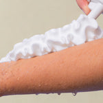 Load image into Gallery viewer, Person applying white foam to a arm against a beige background
